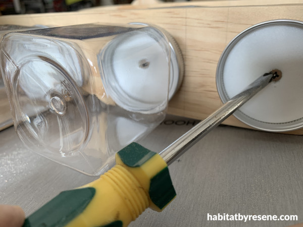 Wood with a jar lid being screwed to it with a screwdriver