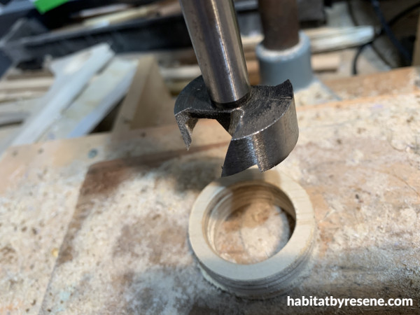 A drill cutting a circle into a round piece of wood to make a ring